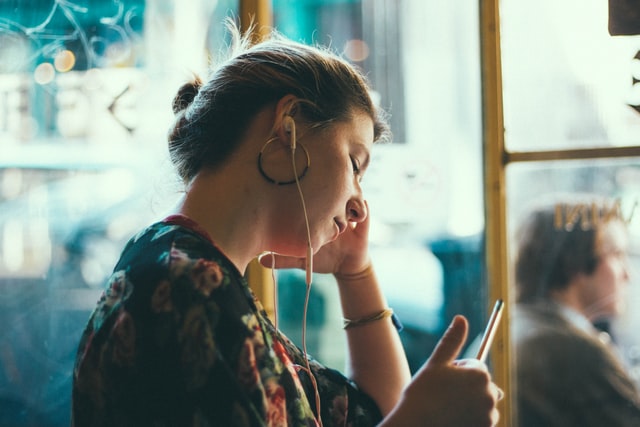 Woman looks tiredly at her phone with earbuds in her ears.