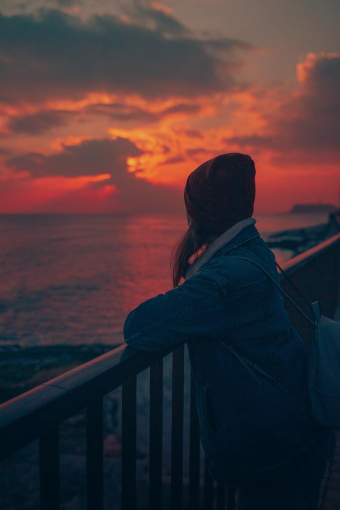 Woman leaning against railing watching a sunset over water.